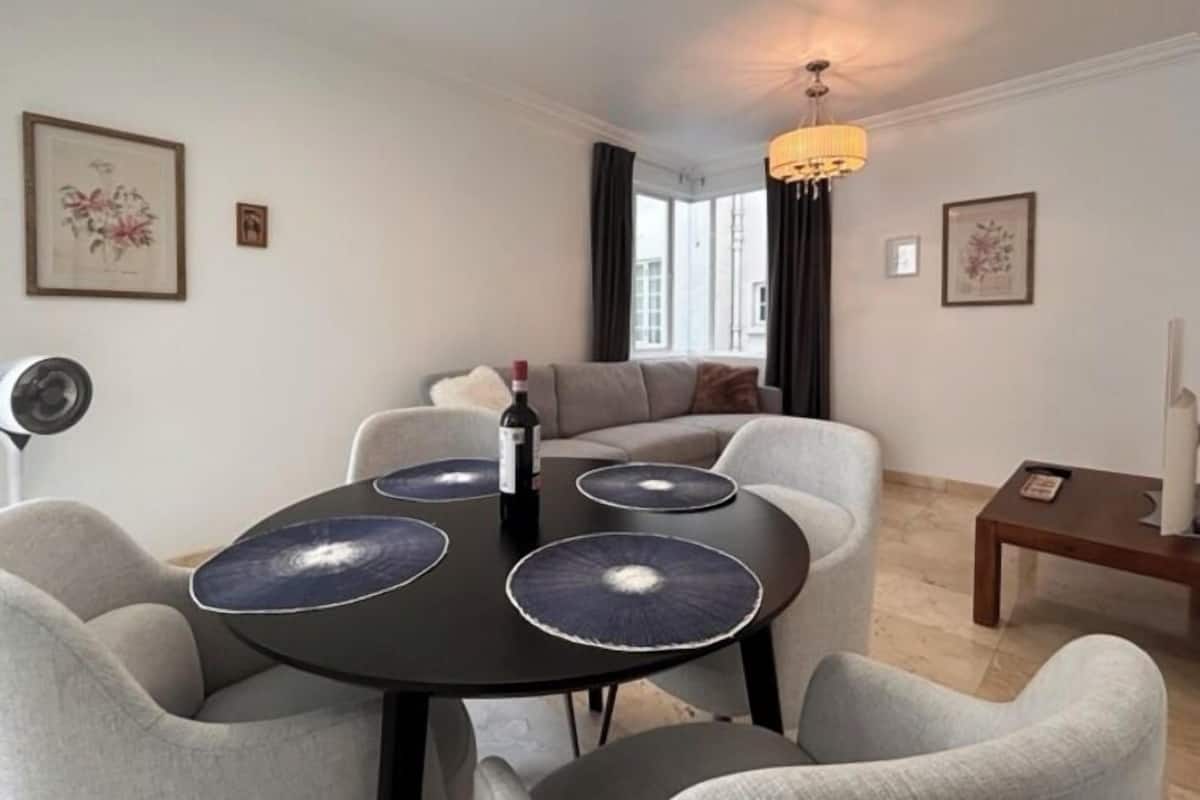 Ein modernes Wohnzimmer mit einem runden Tisch, grauen Sesseln, einer Couch und einer Deckenleuchte.