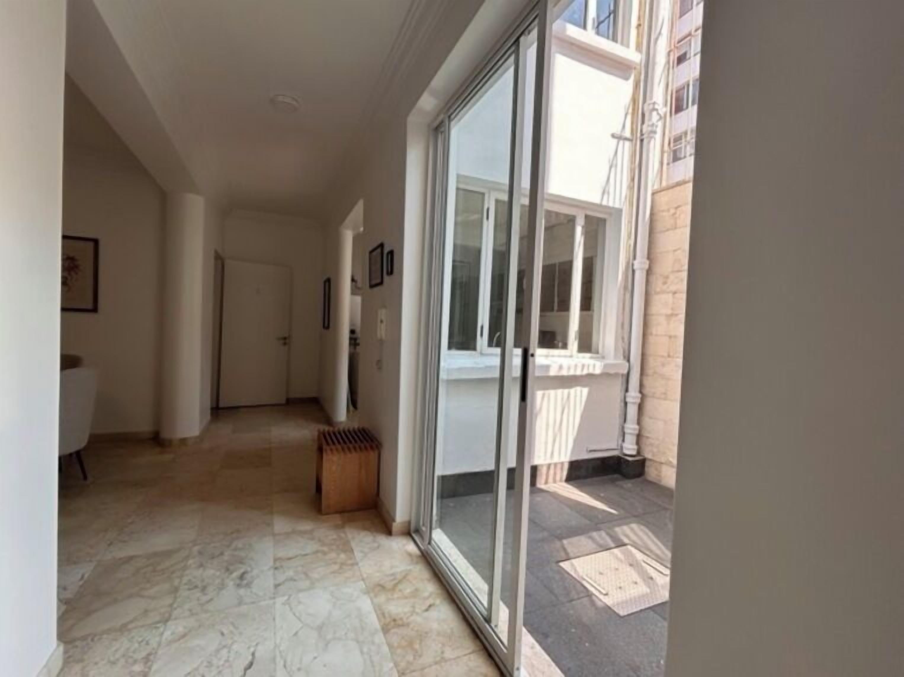 A hallway with a tiled floor leading to a glass door, a small wooden bench, and a white door in the background.