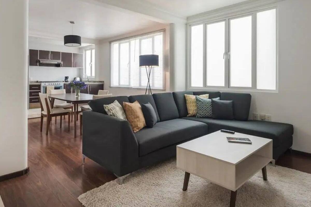 Ein modernes Wohnzimmer mit einem dunklen Sofa, einem weißen Couchtisch und einem Essbereich mit Tisch und Stühlen.