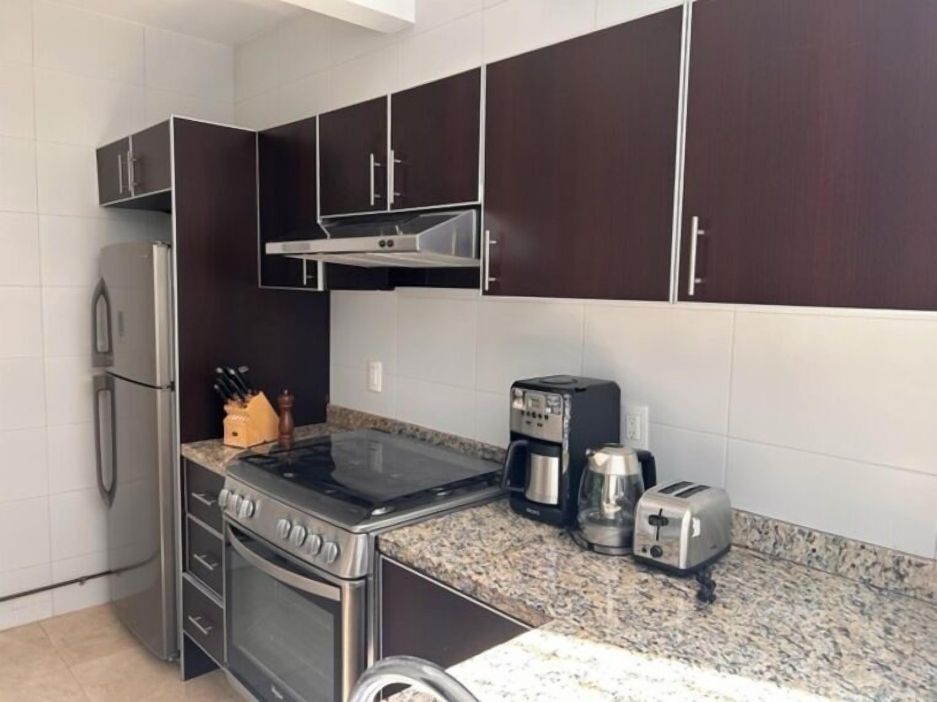 Une cuisine avec des meubles de couleur sombre, un réfrigérateur en acier inoxydable, une cuisinière, une machine à café et un grille-pain.