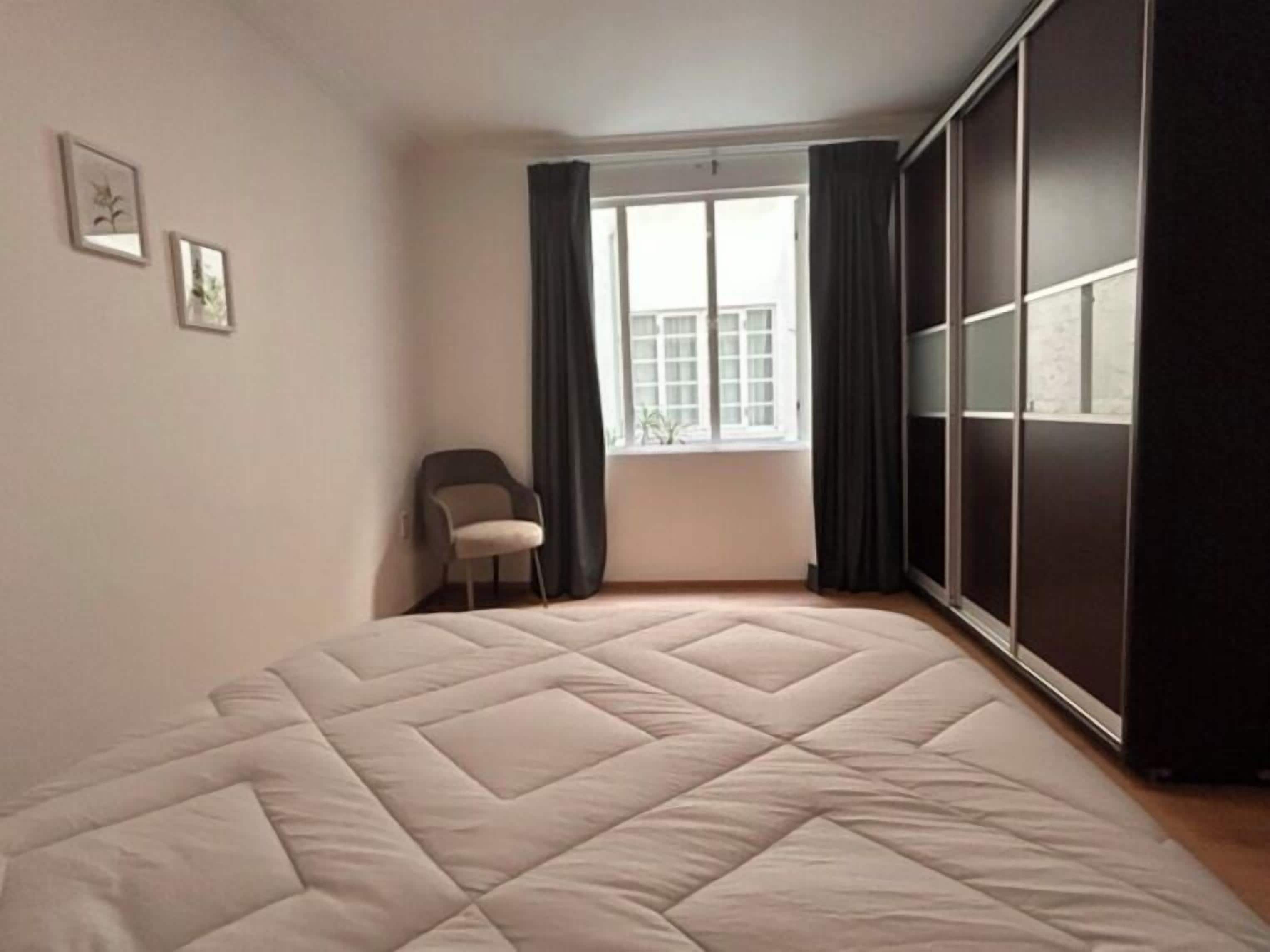 Un dormitorio con cama, una silla, un ventanal y un armario.