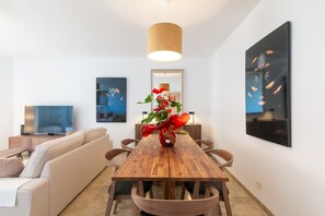 Un salon moderne avec une table à manger en bois, un canapé, un téléviseur et des œuvres d’art accrochées aux murs.