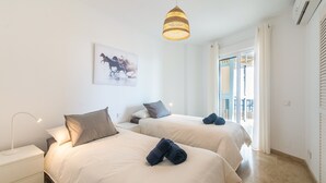 Ein Hotelzimmer mit zwei Betten, einer Hängelampe, einem Wandbild und einem Fenster mit Vorhängen.