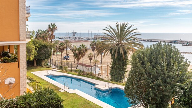 Ein Pool mit Blick auf das Meer, Palmen und ein Gebäude mit Balkonen.