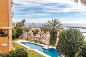 A swimming pool with a view of the sea, palm trees, and a building with balconies.