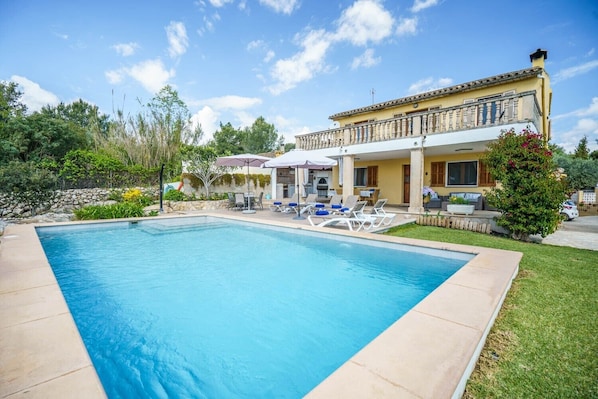 Une piscine avec des chaises longues, un patio couvert et une maison dotée d’un balcon.
