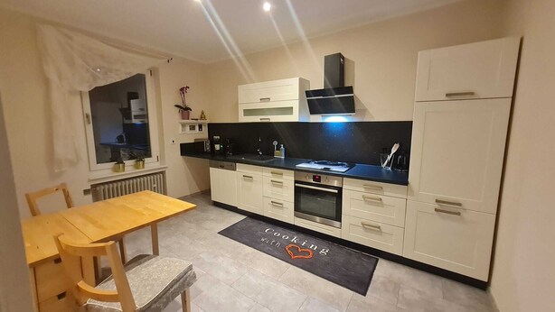 A compact kitchen with white cabinetry, a black countertop, and a built-in oven. - Charmante 2-zimmer-wohnung (Siegen)