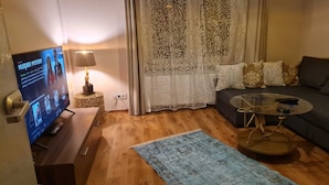 A living room with a flat-screen TV, a round coffee table, a sofa, and a patterned rug. - Charmante 2-zimmer-wohnung (Siegen)