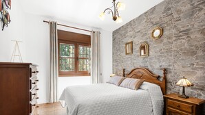 Une chambre à coucher avec un lit, une table de chevet en bois, un mur en pierre et une fenêtre avec des rideaux.