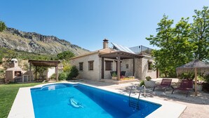 Une piscine avec une maison en pierre, un espace salon extérieur et un paysage montagneux en arrière-plan.