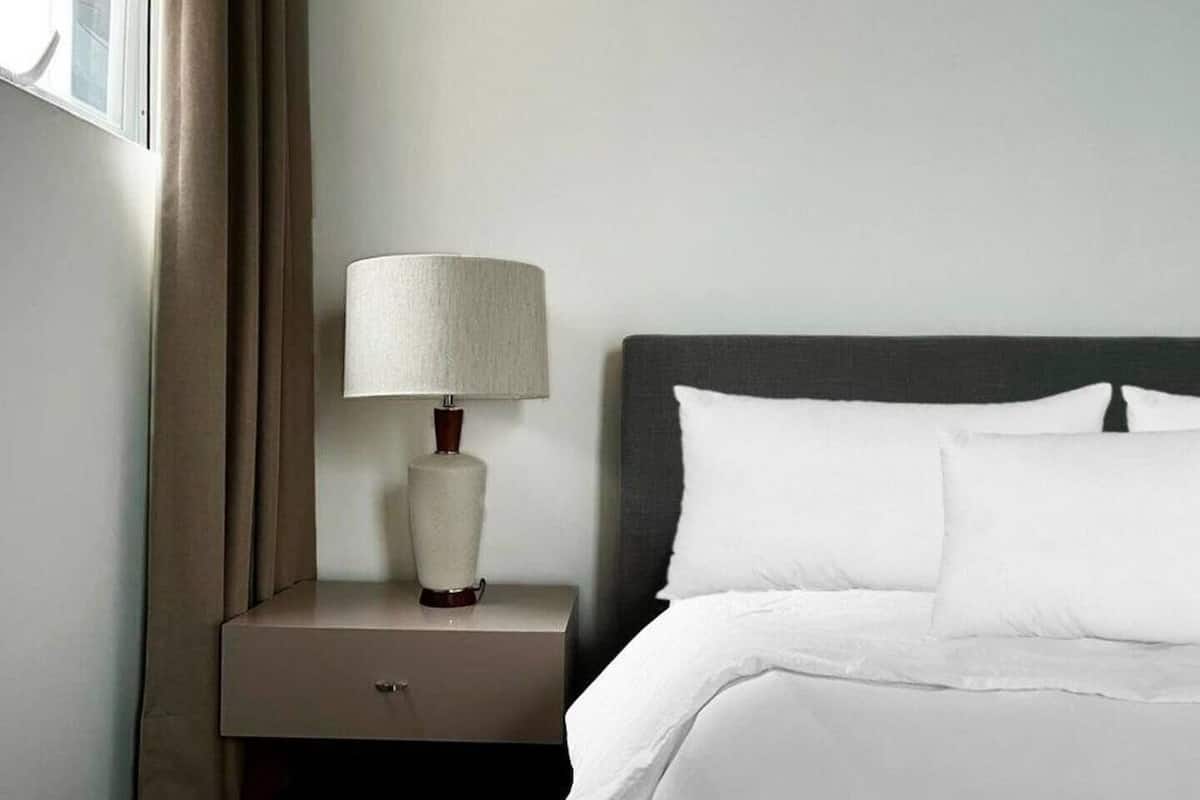 Habitación de hotel con cama, mesita de noche con lámpara y ventana con cortinas.
