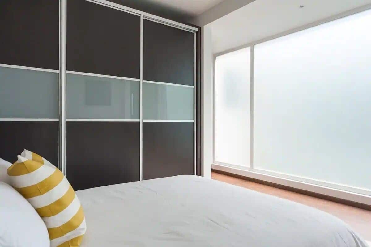 Un dormitorio con cama, armario y un ventanal grande.