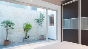 A modern bedroom with a large window, a bed, and three potted plants. - Condesa Residence Amsterdam 181 (Mexico City)