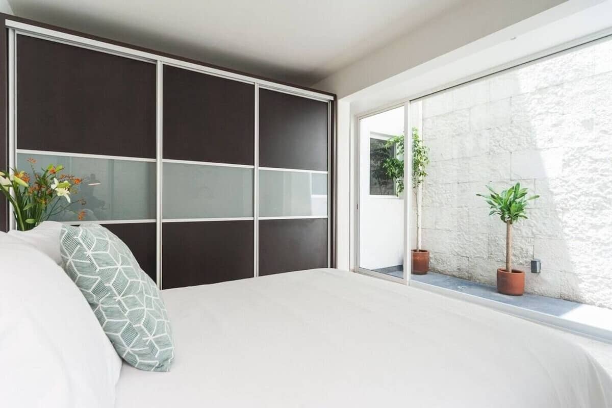 Un dormitorio con una cama grande, un armario correderas oscuro y vistas al exterior mediante una puerta corredera.
