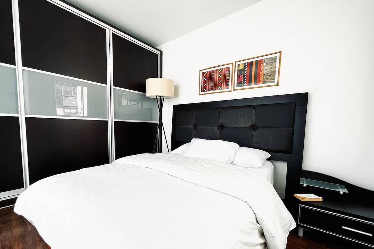 Un dormitorio moderno con una cama grande, cabecera negra, mesita de noche y lámpara de pie.