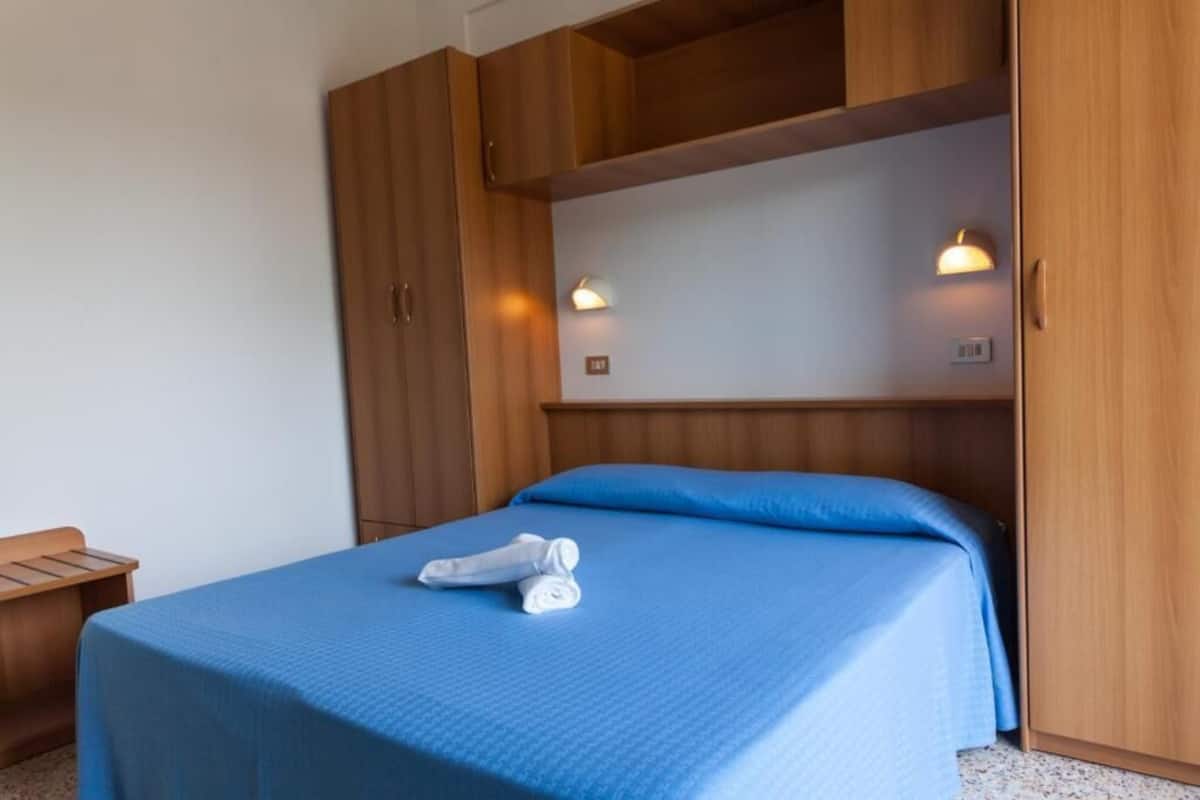 A bedroom with a bed, wooden wardrobe, and two wall-mounted lights.