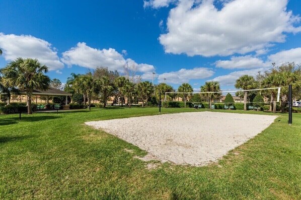 A volleyball court with a net, surrounded by green grass and palm trees. - Cinderella's Castle - Disney Themed Townhome (Kissimme)