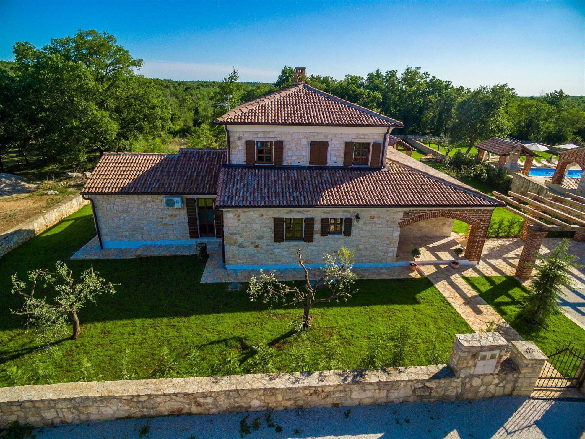 A two-story stone house with a tiled roof, surrounded by a well-maintained lawn and a stone wall.