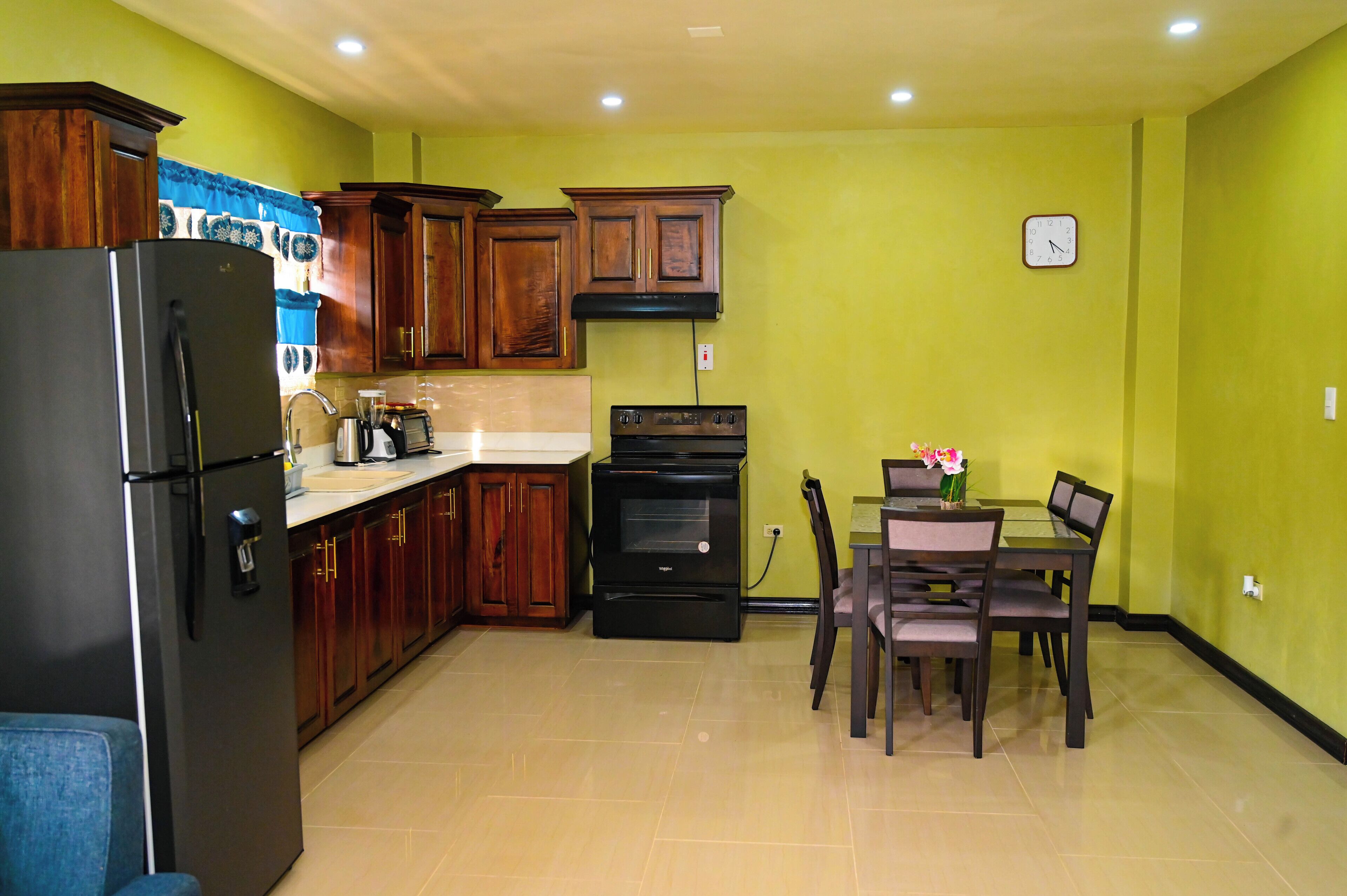 Una cocina con armarios de madera, un refrigerador negro, una estufa y una mesa de comedor con sillas.