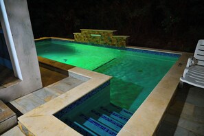 Uma piscina com borda azulejada, uma parede de pedra e uma espreguiçadeira.