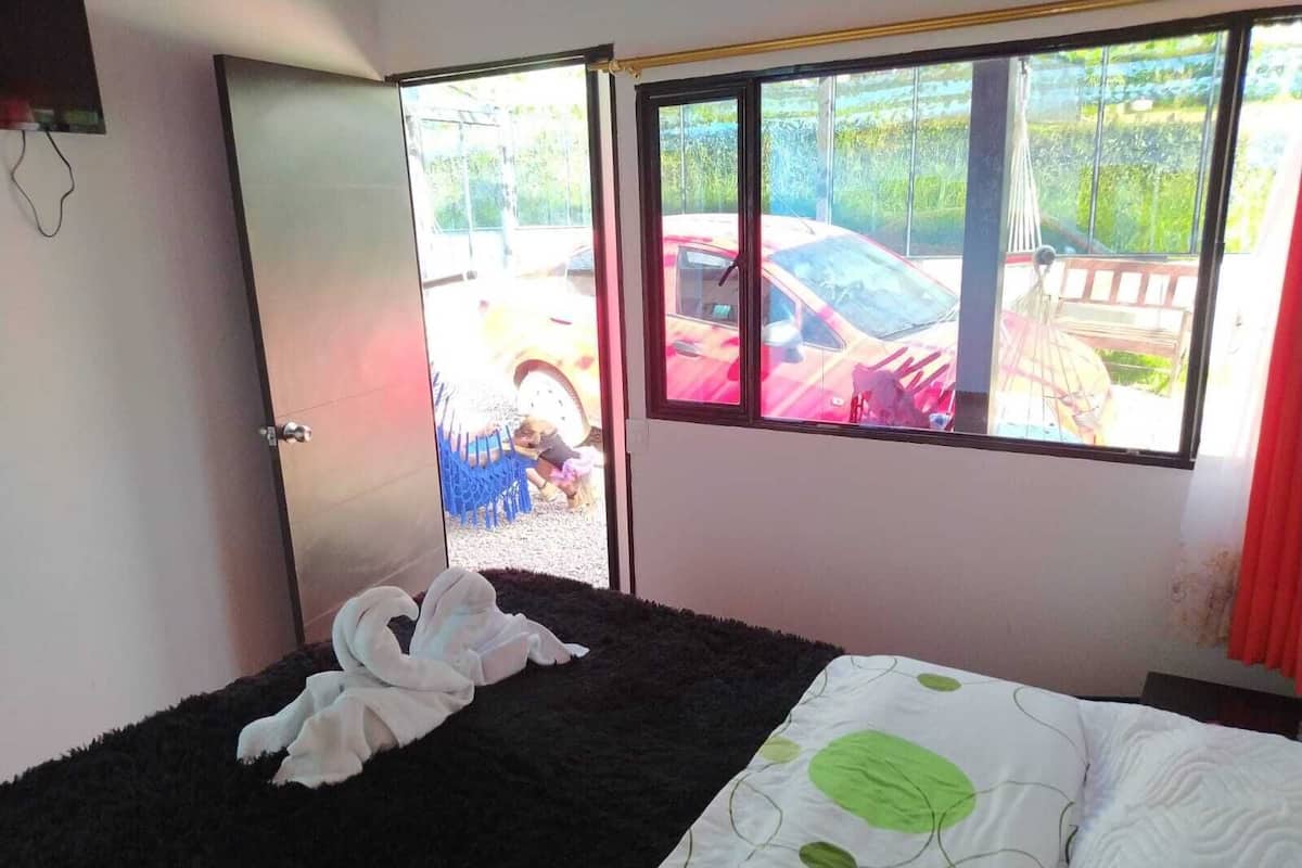 A bedroom with a bed, a window with a view of parked cars, and a door.
