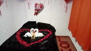 Een kamer met een bed belegd met een zwarte deken, een hartvormige decoratie op het bed en een bord met de tekst 'LOVE' op de vloer.