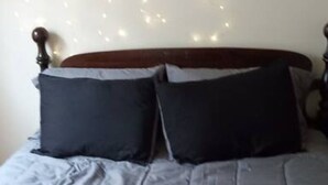 A bed with a grey duvet and two dark pillows, a wooden headboard, and a wall clock.