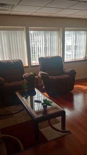 Una sala de estar con un sofá de cuero marrón, un sillón marrón y una mesa de centro de vidrio con plantas.