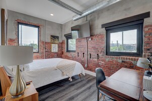 Habitación de hotel moderna con paredes de ladrillo visto, una cama grande, un escritorio con silla y una ventana con vistas a la ciudad.