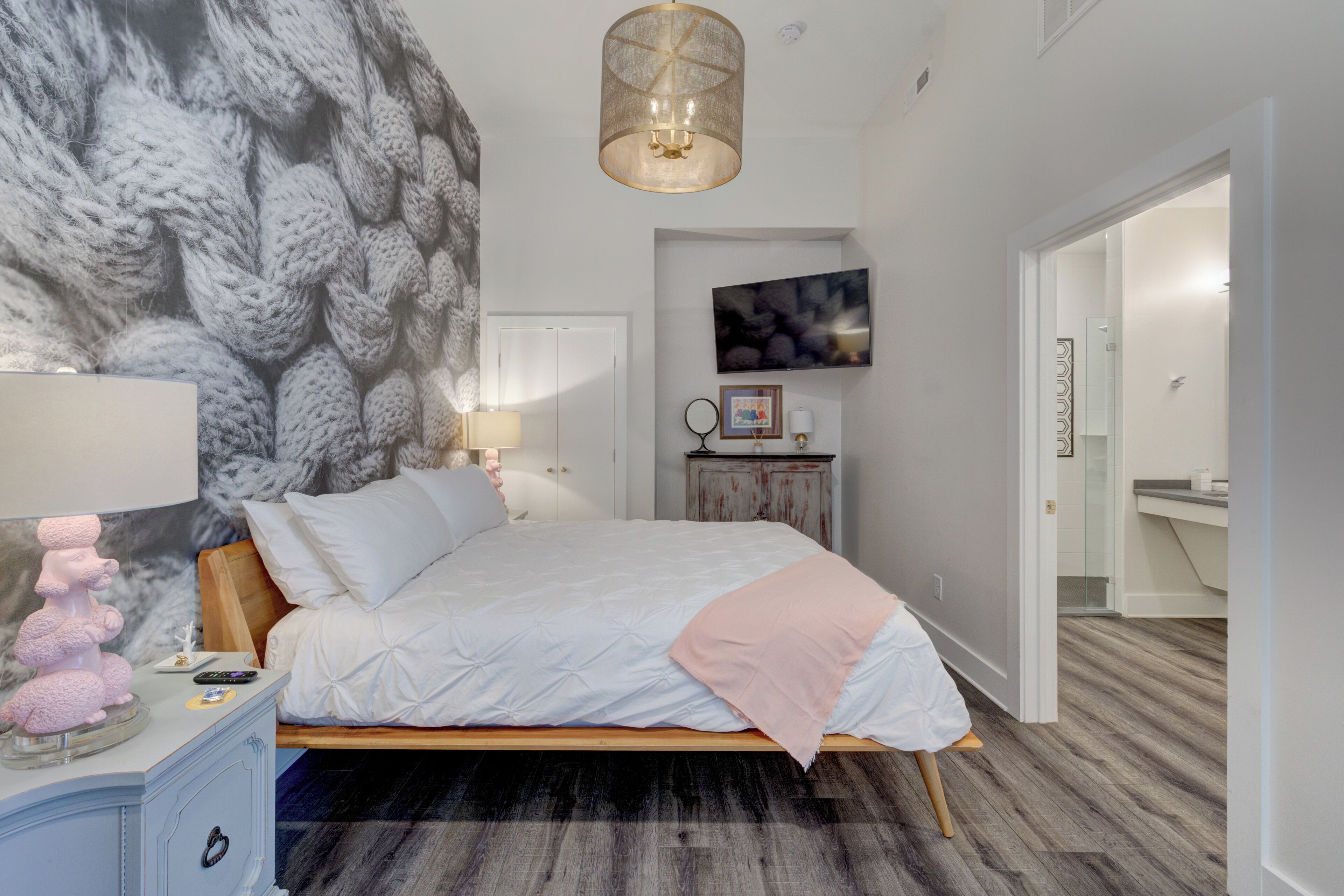 Un dormitorio con cama, mesita de noche, lámpara de pared, cuadro enmarcado y espejo.