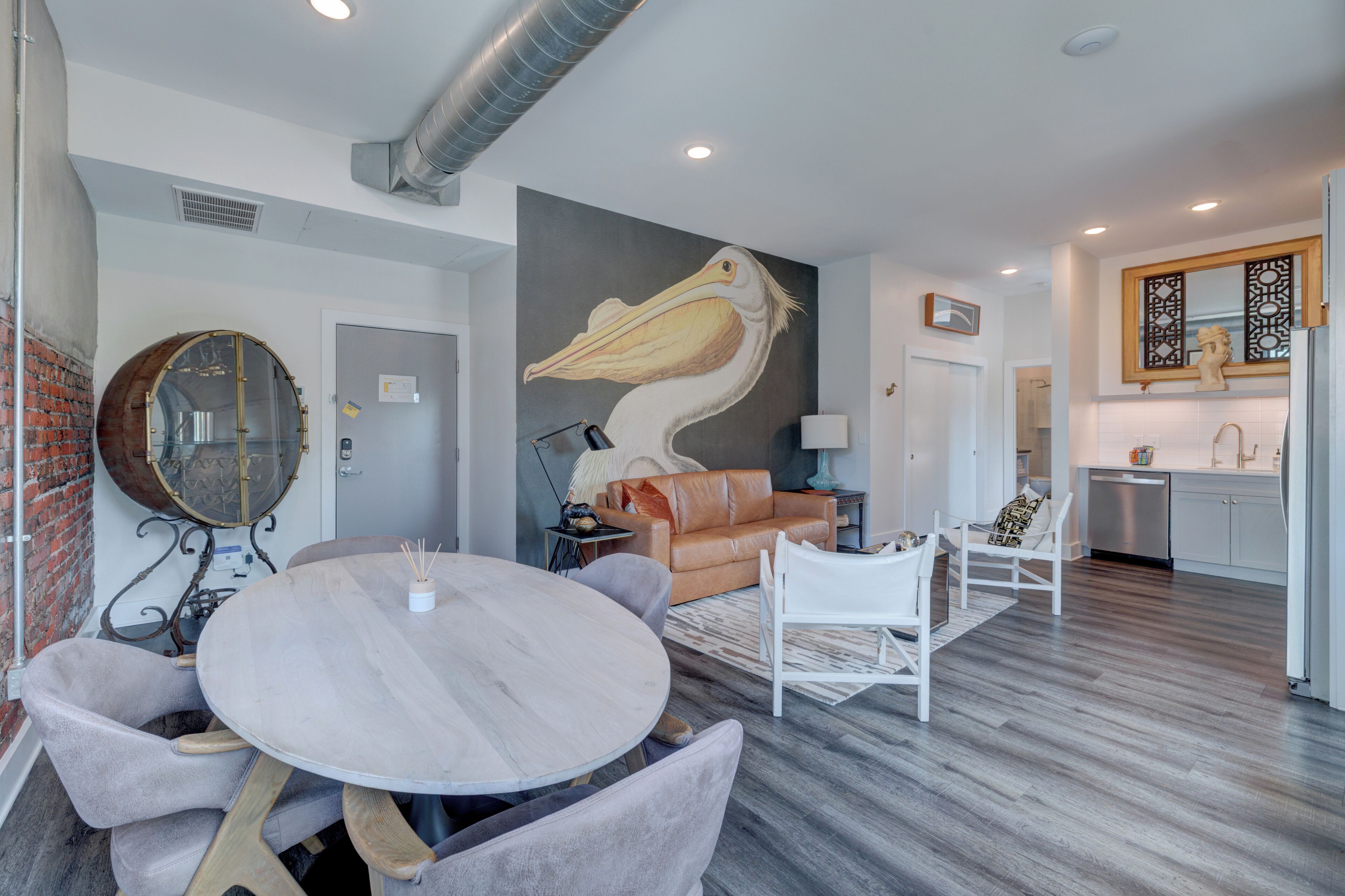 A modern living room with a large mural, a round dining table, and a kitchen area.