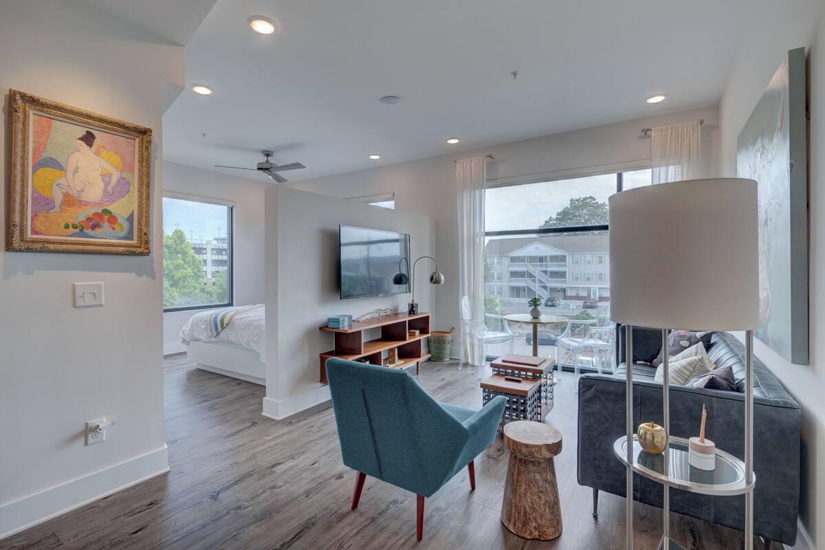 Un salon moderne avec un canapé, un fauteuil turquoise, une table basse et un téléviseur fixé au mur.