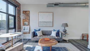 Un salon moderne avec un canapé gris, une table basse ronde en bois et une grande fenêtre.