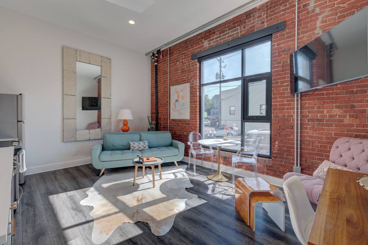 Un salon moderne avec un mur en briques, une grande fenêtre, un canapé, une table basse et un téléviseur.