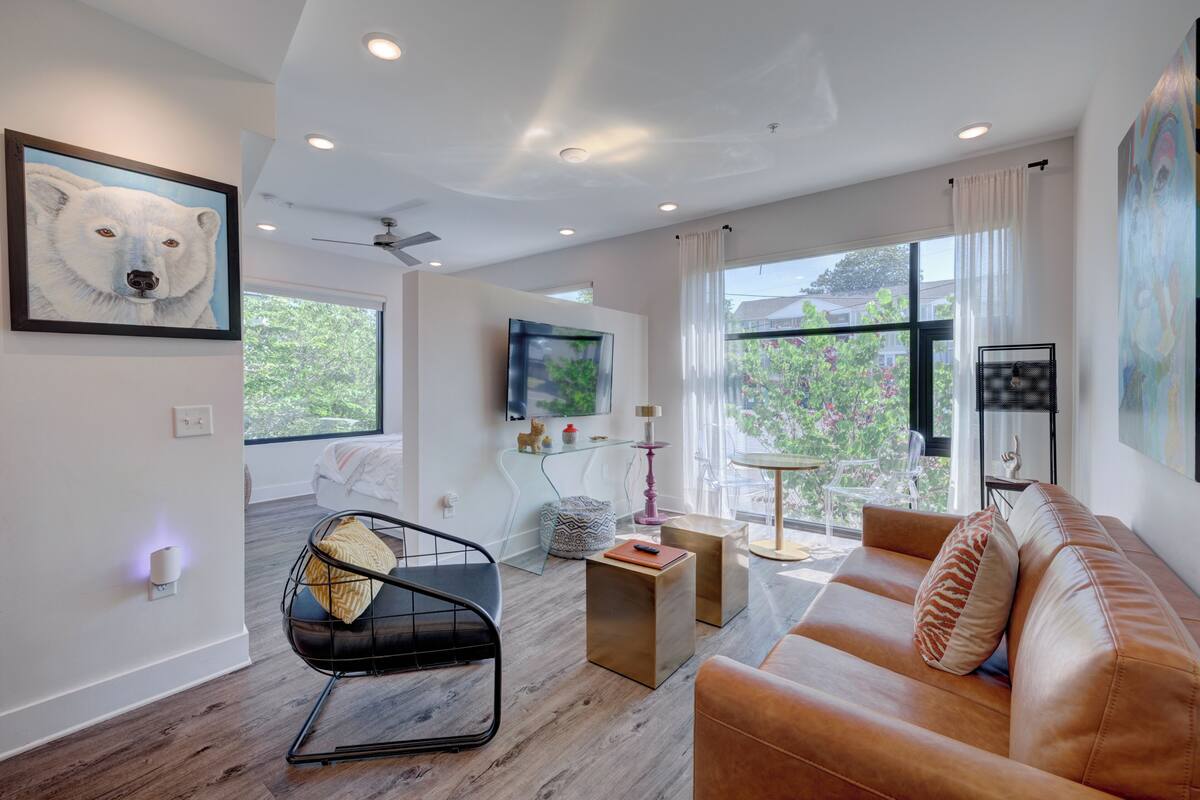 Un salon moderne avec un canapé en cuir, un fauteuil noir et une table basse en bois. Une grande fenêtre offre une vue sur la verdure environnante.