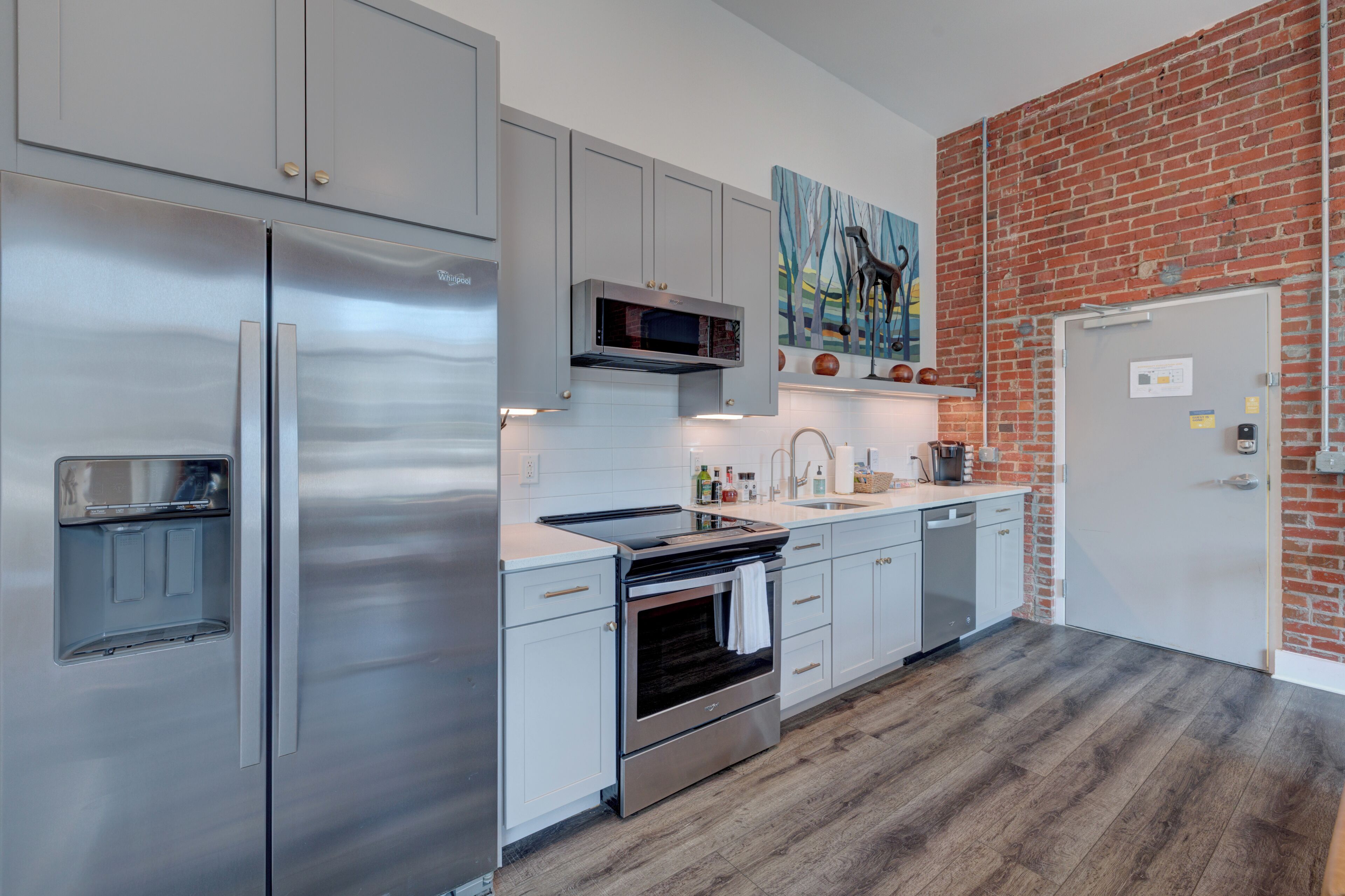 A modern kitchen with stainless steel appliances, white cabinetry, and a brick accent wall.