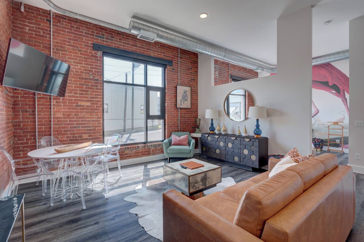 Un salon moderne avec un mur en briques, une grande fenêtre, un téléviseur à écran plat, un canapé, une table basse et un coin repas avec des chaises.