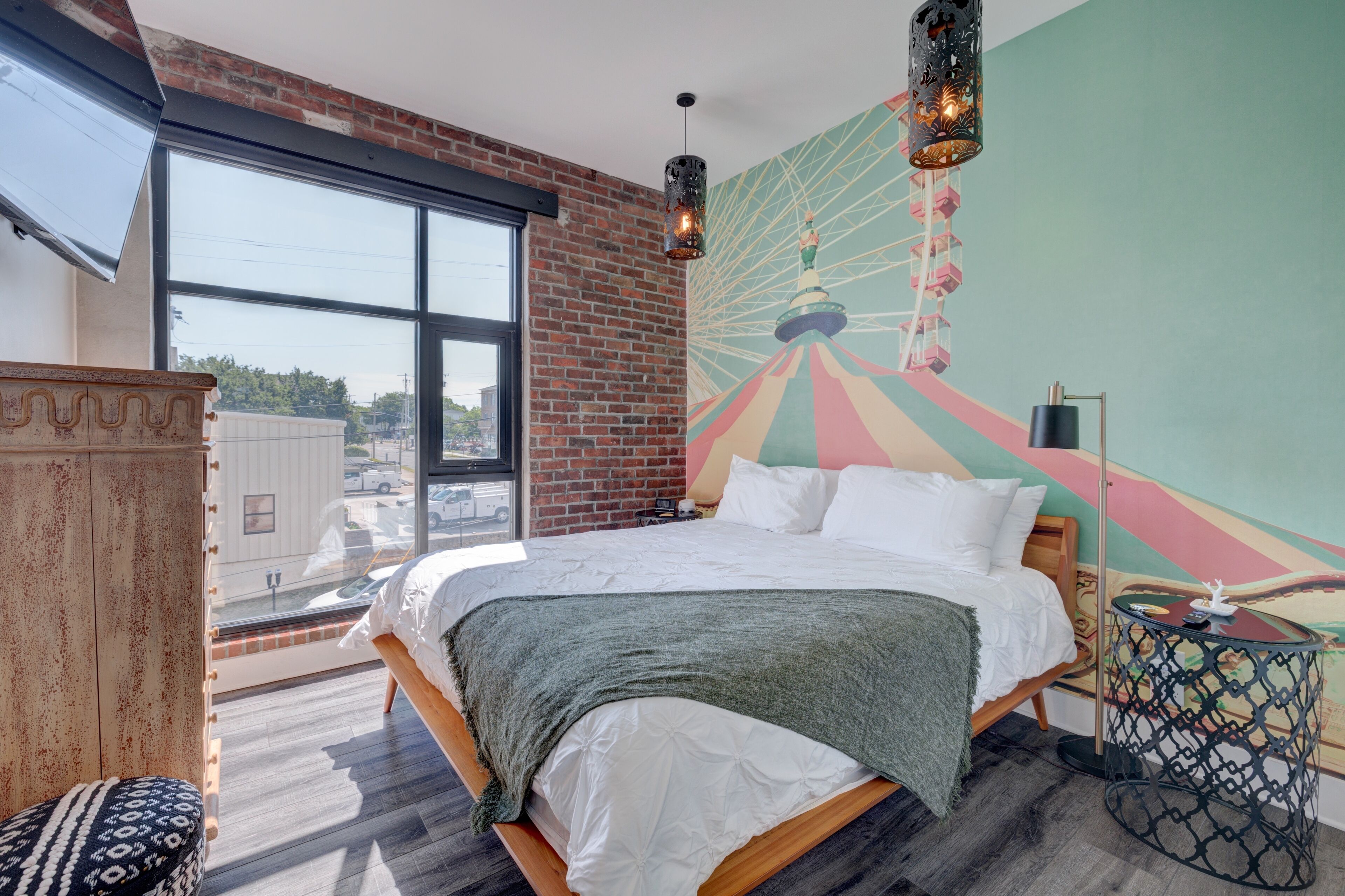 A modern hotel room with a large bed, a view of the city, and a colorful mural on the wall.