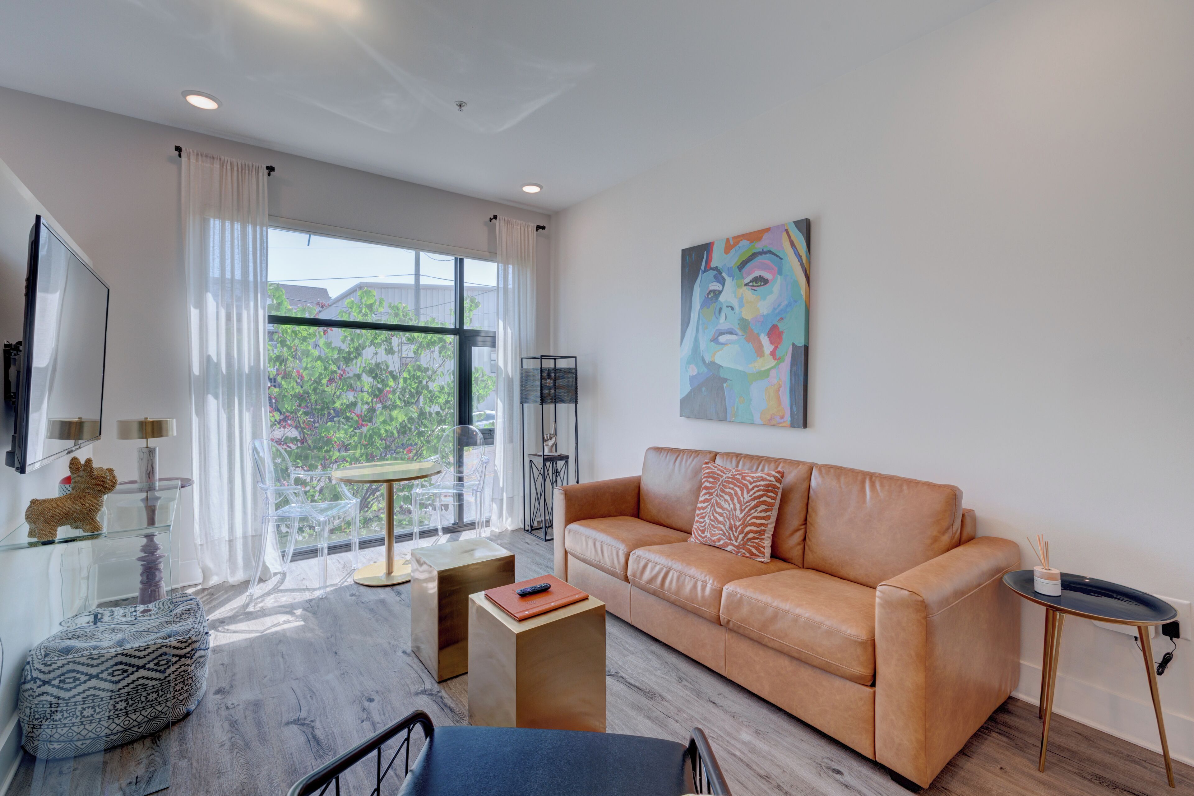 A modern living room with a leather sofa, a glass coffee table, a glass cabinet, and a painting on the wall.