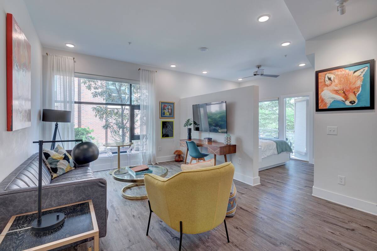 Un salon moderne avec un canapé, un fauteuil jaune, une table basse et un téléviseur.