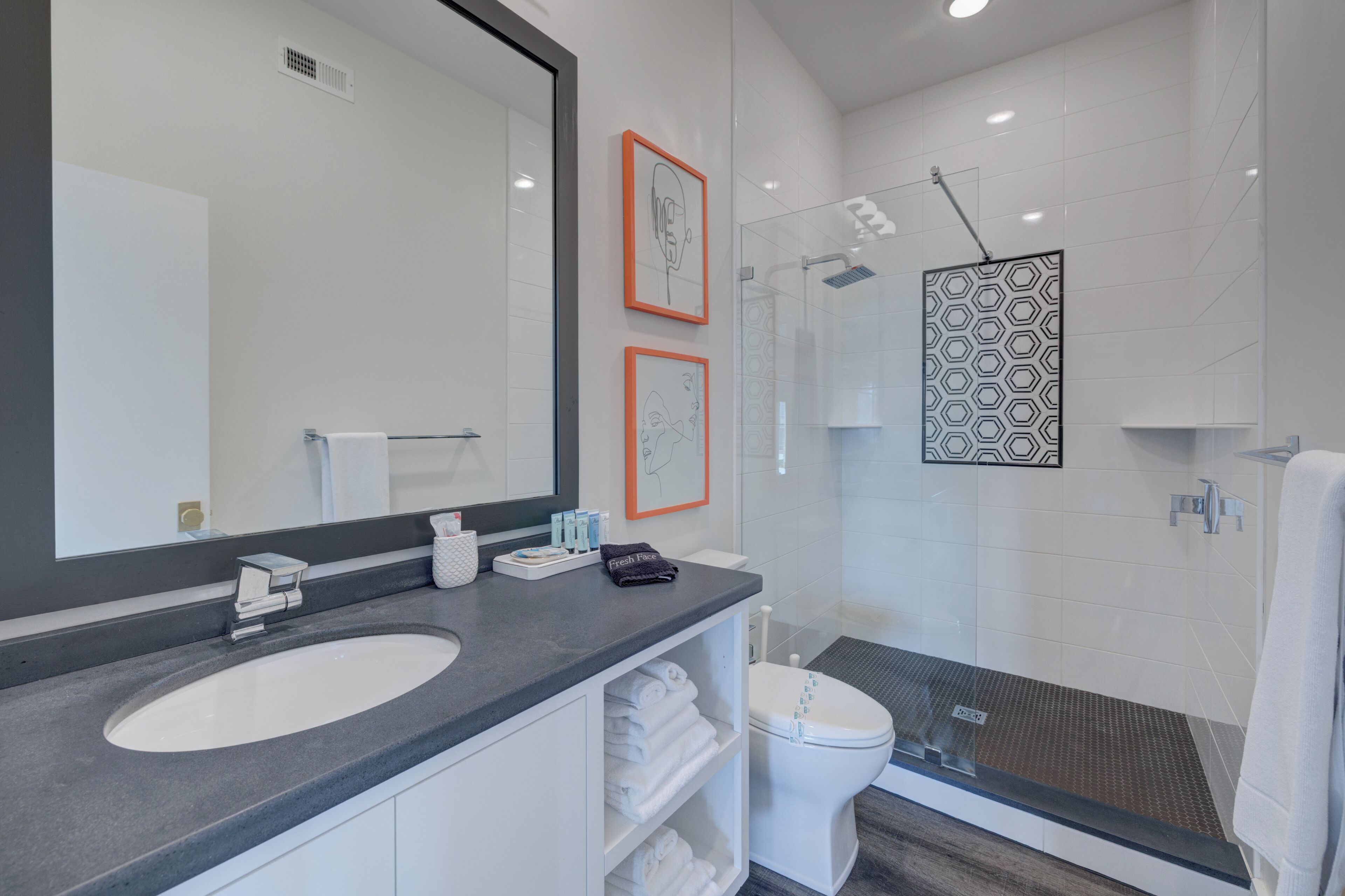 A modern bathroom with a large mirror, a white sink, a toilet, and a shower area.