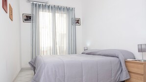 A neatly made bed with a grey duvet, a bedside table with a lamp, and a window with sheer curtains. - Eva Apartment, a stone's throw from the sea (San Vito Lo Capo)