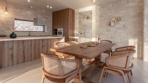 A modern kitchen with a wooden island, stone walls, and a dining area with wicker chairs. - Beachfront Brand New Villa (Ierapetra)