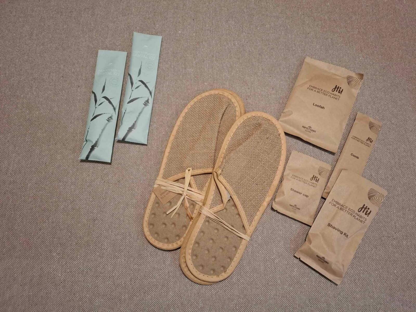 Ett par flätade sandaler, en kam, en rakapparat och flera små bruna papperspåsar med texten ”Hej” och ”anamma miljövänliga vanor för en bättre planet”.