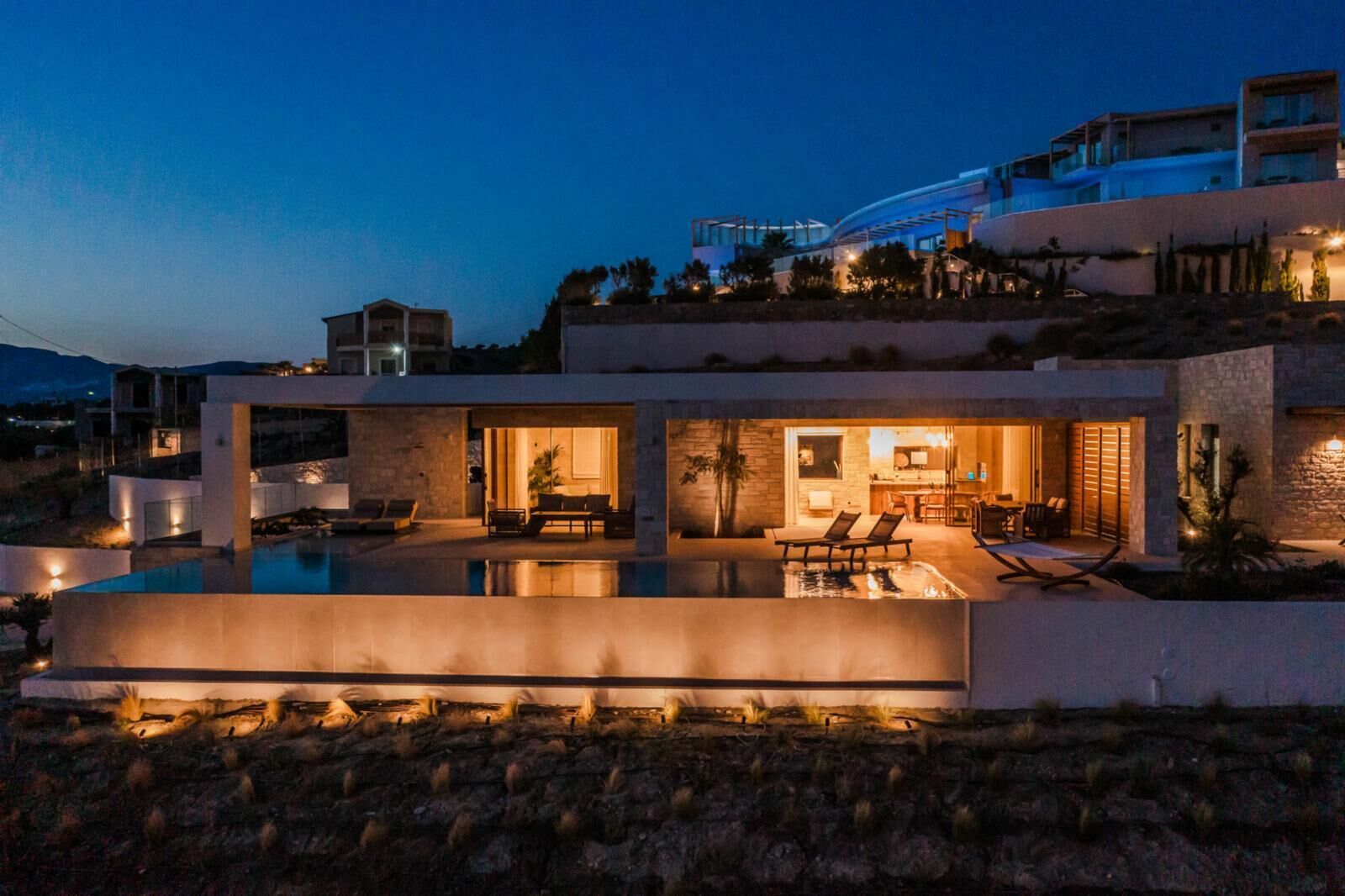 Una casa moderna de varios pisos con piscina, mobiliario exterior y un interior bien iluminado.