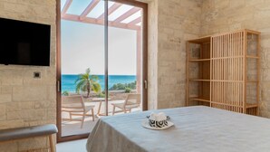 Une chambre avec un lit, un téléviseur fixé au mur et une vue sur la plage, accessible par une porte-fenêtre coulissante.