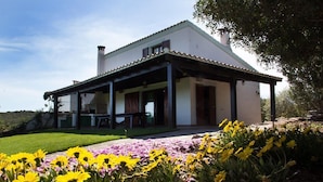 A single-story house with a covered patio, a lawn, and a variety of flowers in the foreground. - Villa "Olga" with Sea View, Private Terrace & Wi-Fi (Carloforte)