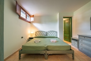 Une chambre à coucher avec un lit, des tables de chevet, une commode, une porte verte et une fenêtre donnant sur un beau paysage.