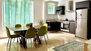 Una cocina moderna con comedor, ventanas amplias y vista a árboles.