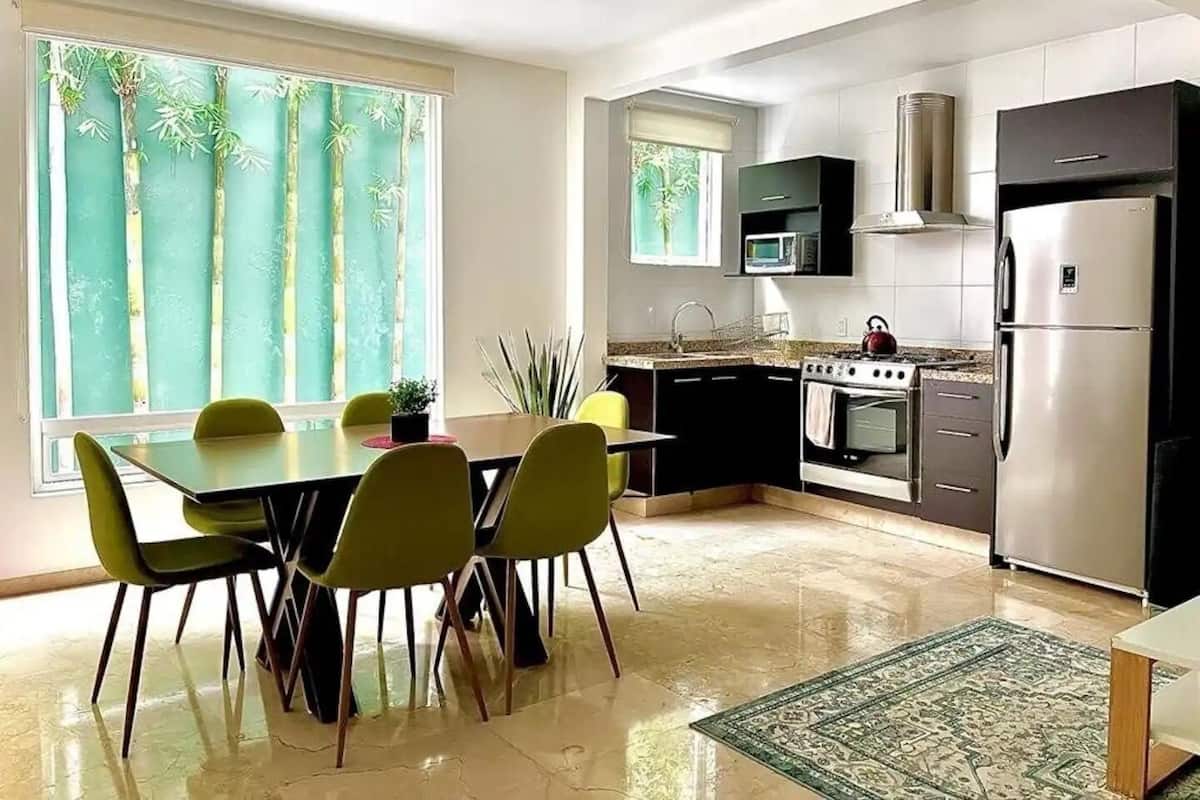 Een moderne keuken met een eethoek, grote ramen en uitzicht op bomen.